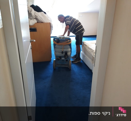 אדם משתמש במכונת ניקוי שטיחים בחדר שינה